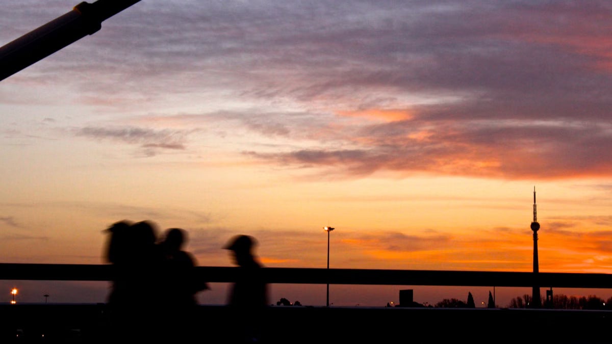 Silhouetted people walking against a vibrant Johannesburg sunset backdrop with cloudy sky.
